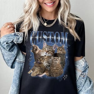 May include: Black t-shirt with a graphic of five cats in a galaxy print. The text "CUSTOM" is printed in blue with a glittery effect.