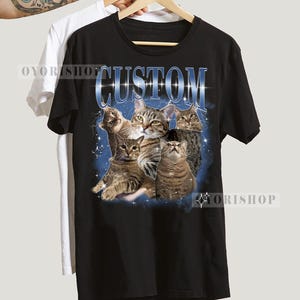 May include: Black t-shirt with a graphic print of a group of cats in a galaxy-like background. The text "CUSTOM" is printed in white letters above the cats.