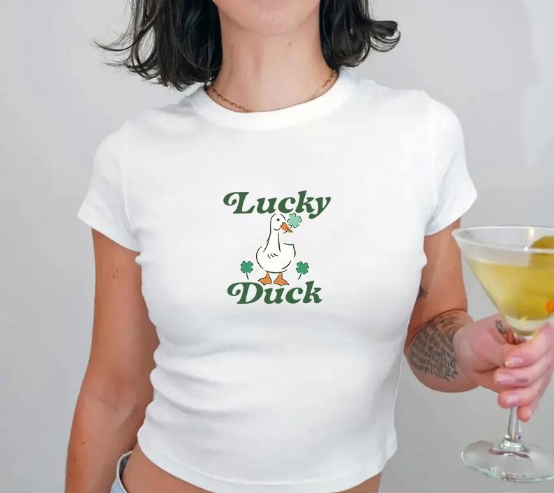 May include: White cropped t-shirt with a green and white cartoon duck holding a shamrock and the text "Lucky Duck" in green.