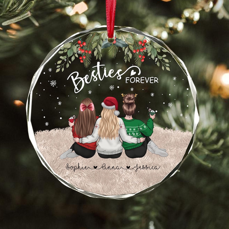 Pu&ograve; includere: Un ornamento natalizio rotondo e trasparente con la scritta "Besties Forever" e tre figure. Le figure sono sedute, di spalle allo spettatore, e indossano maglioni e un cappello da Babbo Natale. I nomi "Sophie", "Anna" e "Jessica" sono sotto.