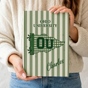 May include: A personalized notebook with a green and white striped background. The notebook features the text "OHIO UNIVERSITY" at the top and a pennant with "OU" in the center. The name "Charles" is written in script below the pennant.