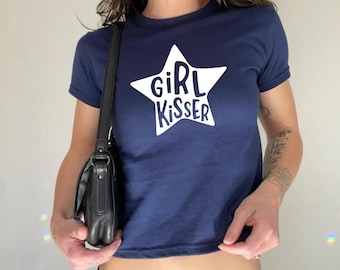 May include: Navy blue crop top with a white star graphic. The star contains the words "GIRL KISSER" in a bold, sans-serif font. The shirt has short sleeves and a crew neck.