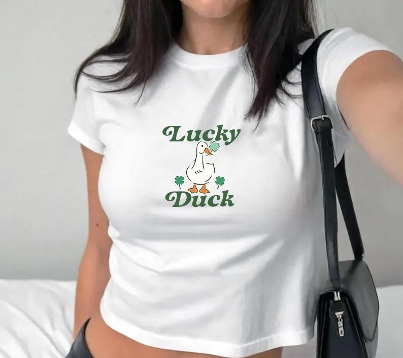 May include: White cropped t-shirt with a green graphic of a duck holding a four-leaf clover and the text "Lucky Duck".
