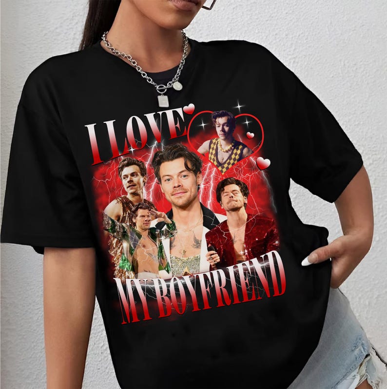 Op de afbeelding: Zwart T-shirt met een grafische print van een man met de tekst "I LOVE MY BOYFRIEND" in rode en witte letters. De grafiek bevat ook bliksem en harten.