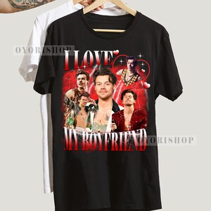 Op de afbeelding: Zwart T-shirt met een grafische print van een groep mannen met de tekst "I LOVE MY BOYFRIEND" in witte letters.