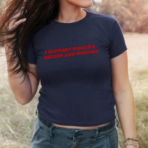 May include: Navy blue t-shirt with the red text "I SUPPORT WOMEN'S RIGHTS AND WRONGS". The shirt is a crew neck style and is made of a soft material. The model is wearing blue jeans.