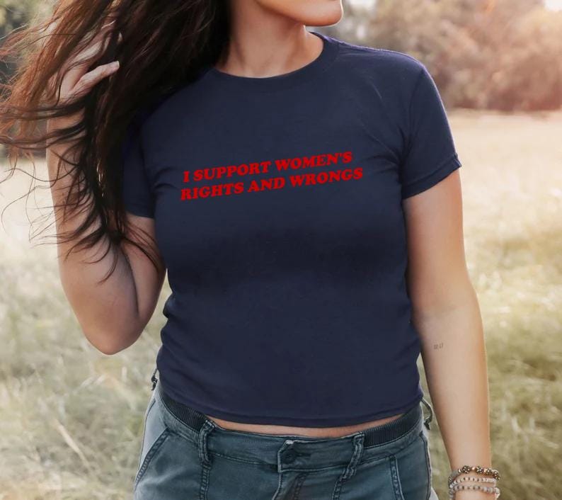 May include: Navy blue t-shirt with the red text "I SUPPORT WOMEN'S RIGHTS AND WRONGS". The shirt is a crew neck style and is made of a soft material. The model is wearing blue jeans.