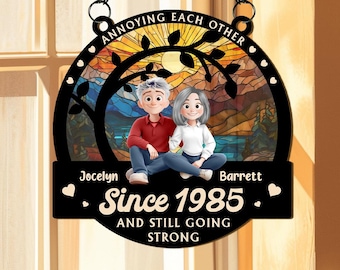 May include: A black metal sign with a stained-glass style background featuring a couple sitting together. The sign reads "Annoying Each Other" and "Since 1985 and Still Going Strong." The names Jocelyn and Barrett are also displayed.