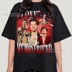 Op de afbeelding: Zwart T-shirt met een grafische print van een collage van afbeeldingen van een man met de tekst "I Love My Boyfriend" in rode en witte letters.