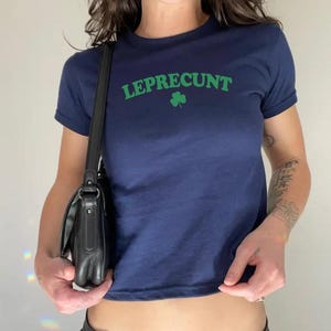 May include: A navy blue cropped t-shirt with the text "LEPRECU*NT" in green letters and a green shamrock.