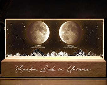 May include: A wooden base with a clear acrylic panel displaying two moons with the names "JAMES" and "SOPHIA" and their birth dates. The text "Random Luck in Universe" is engraved on the wooden base.