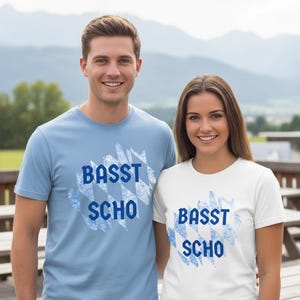 Könnte beinhalten: Zwei Personen tragen passende T-Shirts mit dem Text "BASST SCHO" in Blau. Ein Shirt ist hellblau, das andere ist weiß. Der Text befindet sich über einem blau-weißen bayerischen Rautenmuster.