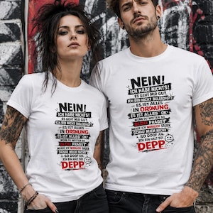 Könnte beinhalten: Zwei Personen tragen weiße T-Shirts mit dem deutschen Satz "NEIN!" und anderem deutschen Text in Schwarz und Rot. Die Shirts haben eine Used-Schriftart und eine Grafik eines Gesichts. Der Hintergrund ist eine Graffiti-Wand.