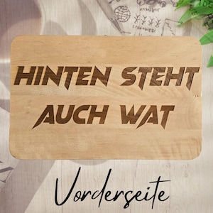 Könnte beinhalten: Ein rechteckiges Holzschneidebrett mit abgerundeten Ecken. Das Brett zeigt den eingravierten Text "HINTEN STEHT AUCH WAT" in fetten, stilisierten Buchstaben. Darunter steht das Wort "Vorderseite" in Schreibschrift.
