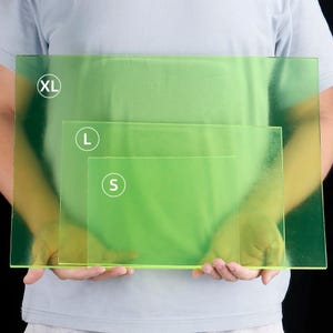May include: Three transparent green rectangular sheets of varying sizes are held up. The largest is labeled "XL", the middle one "L", and the smallest "S". The sheets are held in front of a person wearing a light blue shirt.