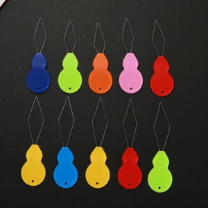 May include: A set of ten needle threaders arranged in two rows. Each threader features a gourd-shaped plastic handle in various colors including blue, lime green, orange, pink, red, and yellow, with a thin diamond-shaped wire loop at the top.