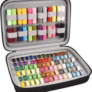May include: A black zippered sewing kit, open to reveal spools of colorful thread and bobbins. The top section holds thread spools secured by elastic bands. The bottom section is filled with a variety of thread bobbins in a rainbow of colors.