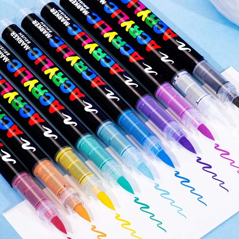 May include: A collection of colorful acrylic brush markers. Each marker has a black barrel with the words "ACRYLIC MARKER BRUSH" in a rainbow of colors. The tips of the markers are visible, with each one creating a wavy line of matching color.