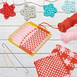 May include: A yellow square weaving loom with pink and orange yarn woven in a grid pattern. Includes two wooden needles, a metal hook, two balls of yarn in orange and pink, and four crocheted star ornaments in red, beige, teal, and light blue.