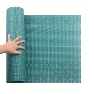 Peut inclure: Un tapis de coupe vert, partiellement enroulé, avec un motif quadrillé et diverses formes pour une coupe précise. Le tapis comporte des mesures en centimètres et est conçu pour les projets d'art et d'artisanat.