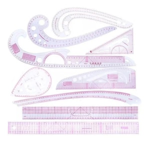 May include: A collection of clear plastic drafting tools, including French curves, rulers, and triangles. The tools have pink grid markings and measurements in inches. Ideal for sewing, pattern making, and design projects.