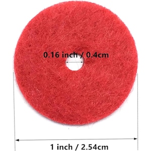 Puede incluir: Un disco de fieltro rojo con un orificio central. El orificio central mide 0,4 cm de diámetro y el diámetro total del disco circular es de 2,54 cm. La textura del material se ve fibrosa y densa.