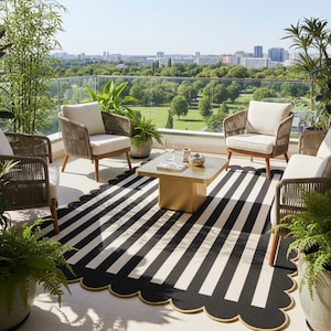 May include: Outdoor patio setting with four woven armchairs, a square gold coffee table, and a black and white striped rug with a scalloped edge. Potted plants and a city view complete the scene.