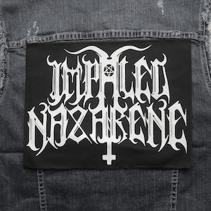 Op de afbeelding: Een zwart denim vest met een zwarte patch die op de achterkant is genaaid. De patch heeft witte tekst die "Impaled Nazarene" luidt in een gotisch lettertype. De tekst wordt omringd door een decoratieve rand.