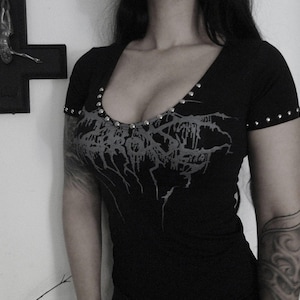 Może przedstawiać: Czarny T-shirt z srebrnym wzorem paska i ozdobnymi ćwiekami. Wzór zawiera napis "MAYHEM" w stylizowanym foncie.