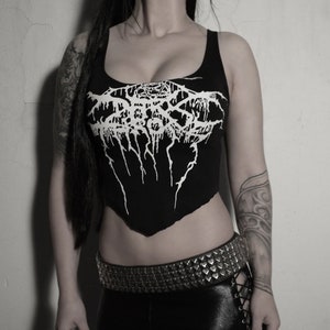 Op de afbeelding: Een zwart crop top met een wit bandontwerp met de tekst "BURzum". Het topje heeft een ronde hals en een licht puntige zoom. Het model draagt een zwarte gespikkeld riem.