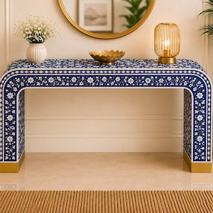 May include: A rectangular console table featuring a deep blue surface with intricate white floral inlay patterns and geometric borders. The table has a curved waterfall design with solid gold-toned metal bases at the bottom of each side panel.
