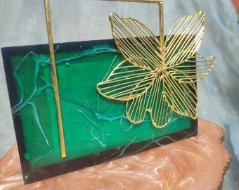 May include: A green and gold decorative box with a wire flower design. The box is on a pink and white marbled surface.