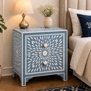 May include: A rectangular two-drawer bedside table featuring a blue and white starburst pattern across the front and sides. The piece has two round white knobs, a flat top surface, and four short legs with a scalloped apron detail at the base.