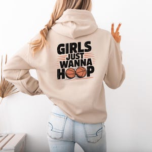 May include: A beige hoodie with a black graphic that says "Girls Just Wanna Hoop" with two basketballs.