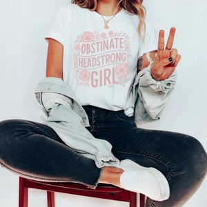 May include: White t-shirt with a pink floral design and the text "Obstinate Headstrong Girl".
