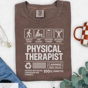 Puede incluir: Camiseta color expreso con texto y gráficos blancos. Muestra "PHYSICAL THERAPIST" con iconos que representan la movilidad, el alivio del dolor, el tratamiento y el fitness. El texto adicional incluye "100% COMMITTED" y "HIGHLY SKILLED".
