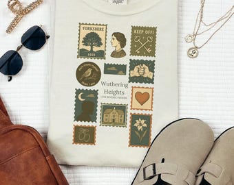 May include: Ivory-colored t-shirt featuring a collection of postage stamp-style illustrations. The stamps include images of a tree, a woman's profile, keys, a bird, a heart, and a house. The text "Wuthering Heights" is also visible.