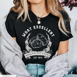 Puede incluir: Camiseta negra con un diseño gráfico blanco que dice "What Excellent Boiled Potatoes Est 1813". El gráfico presenta un dibujo de tres patatas.