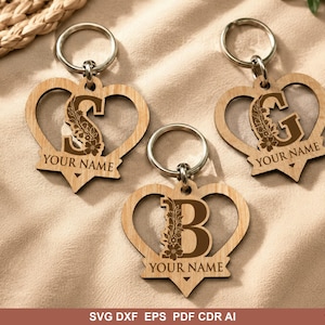 May include: Three light-colored wooden heart-shaped keychains with metal rings. Each keychain features a large dark brown letter S, G, or B decorated with floral patterns. Below each letter, the text YOUR NAME is engraved on a banner.