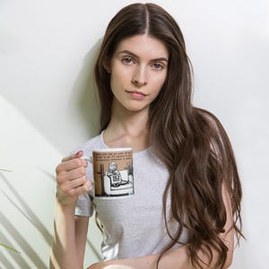May include: White ceramic mug featuring a cartoon cat sitting in a chair with a laptop. The mug has a brown border and text that reads, "Dawn's juice was no good, yet I'm invited to the next meeting to kill the managing director in town."