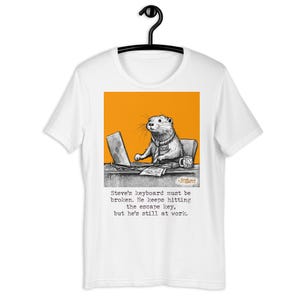 Könnte beinhalten: Weißes T-Shirt mit einer Cartoon-Illustration eines Bibers, der eine Krawatte trägt und an einem Laptop arbeitet. Der Text auf dem Shirt lautet: "Steves Tastatur muss kaputt sein. Er drückt immer wieder die Escape-Taste, aber er ist immer noch bei der Arbeit."