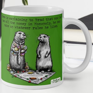 May include: White ceramic coffee mug with a green background and a cartoon illustration of two otters playing a board game. The text on the mug reads "Sheve is explaining to Brad that now he has all the money in Monopoly, he can make up whatever rules he likes." The mug also has the text "In örter News" at the bottom.