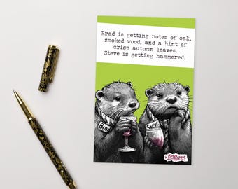 May include: A humorous greeting card featuring two otters, Brad and Steve, with wine glasses. The card has a green and white background with the text "Brad is getting notes of oak... Steve is getting hammered." A decorative pen is also visible.