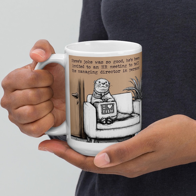 May include: White ceramic mug featuring a cartoon otter sitting on a couch, holding a sign that says "I love fish." The mug has text that reads "Steve's joke was so good, he's been invited to an HR meeting to tell the managing director in person."