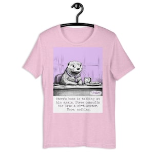 Könnte beinhalten: Hellrosa T-Shirt mit einem Cartoon-Otter, der ein Namensschild mit der Aufschrift "Steve" trägt. Der Otter sitzt an einem Schreibtisch mit einer Kaffeetasse und einem Keks. Der Text auf dem Shirt lautet: "Steves Chef redet wieder mit ihm. Steve konsultiert sein Give-a-sh*t-ometer. Nope. nichts."