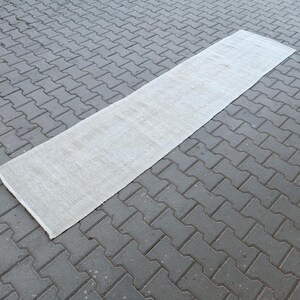 Puede incluir: Una alfombra de pasillo blanca colocada sobre un patio de adoquines grises.