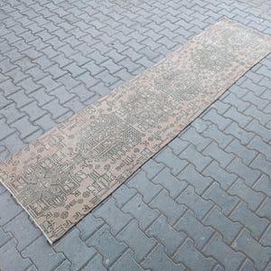 May include: A rectangular, vintage-style rug with an intricate geometric pattern in shades of beige and gray. The rug is placed on a gray brick surface, showcasing its detailed design and aged appearance. Ideal for adding a touch of classic elegance to any space.