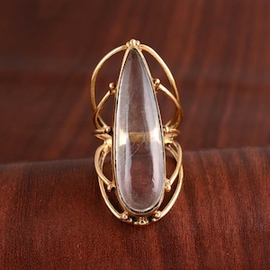 May include: A gold ring with a clear teardrop-shaped stone set in a cage-like design.