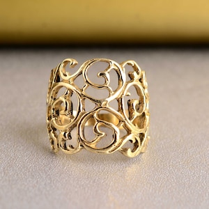May include: A gold filigree ring with a delicate, intricate design. The ring is made of a single piece of metal and has a wide band.