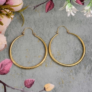 May include: A pair of gold hoop earrings with a textured surface. The earrings are large and circular.